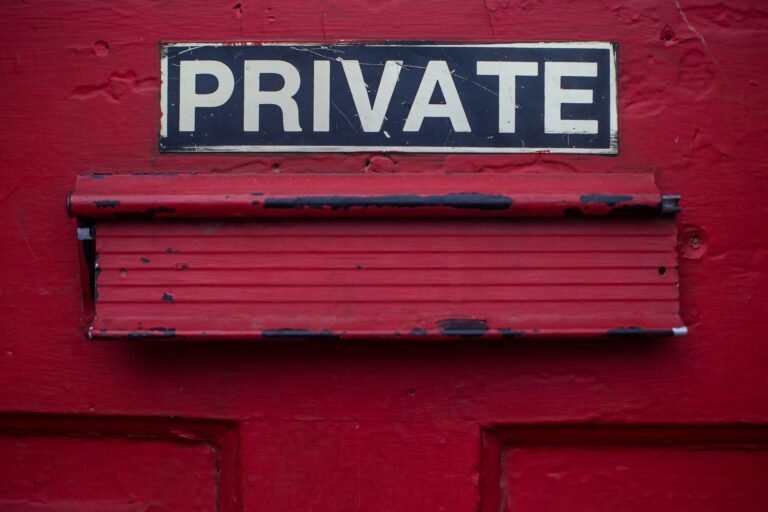 Close-up of a black and white "PRIVATE" sign mounted on an old, red, weathered door