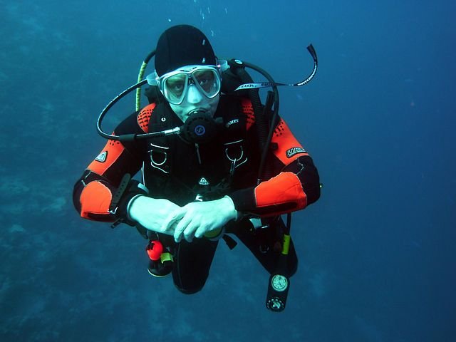 A scuba diver in a horizontal position practicing neutral buoyancy with arms folded, demonstrating ideal trim and breath control underwater.